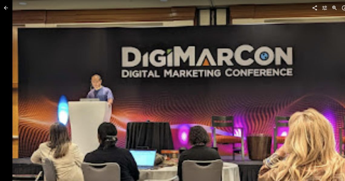 Dennis Yu presenting at the podium on the DigiMarCon Digital Marketing Conference stage with audience watching