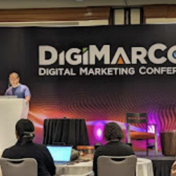 Dennis Yu presenting at the podium on the DigiMarCon Digital Marketing Conference stage with audience watching