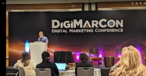 Dennis Yu presenting at the podium on the DigiMarCon Digital Marketing Conference stage with audience watching