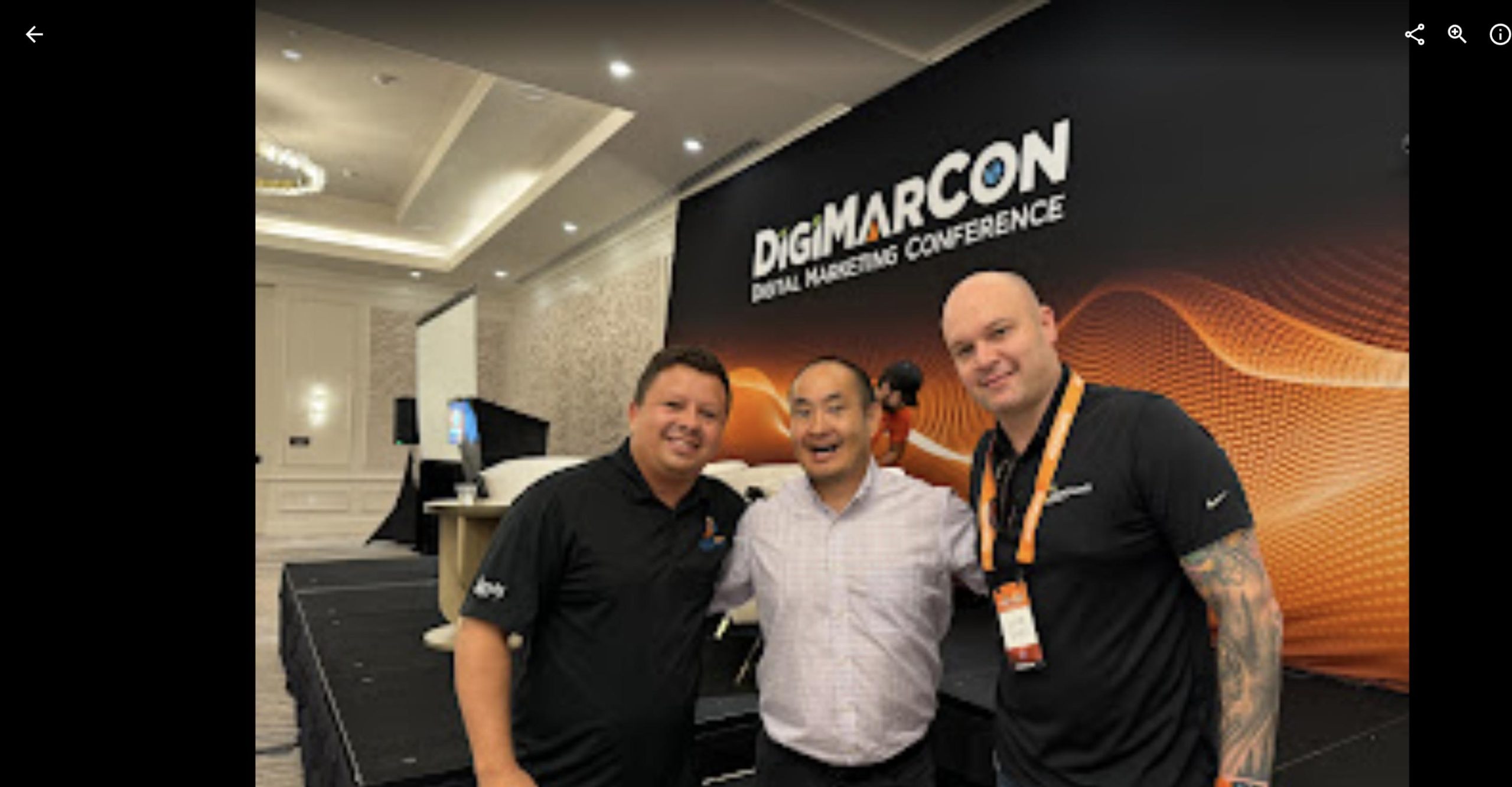 Dennis Yu smiling with two fellow attendees in front of the DigiMarCon conference backdrop.